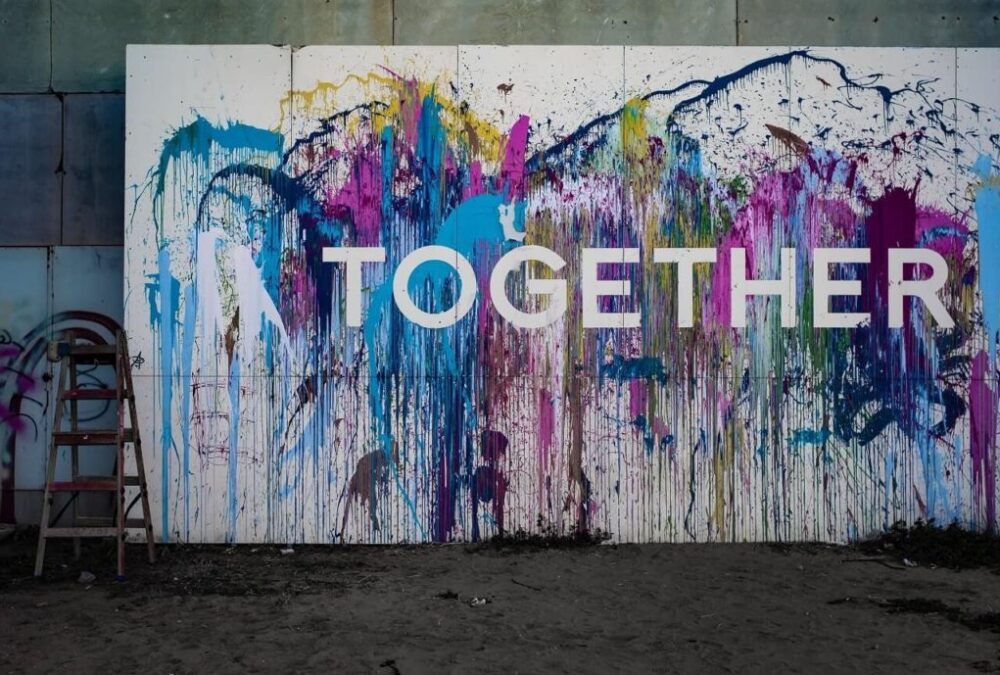 Image, the word "together" in white paint over a Jackson Pollock-style paint-splash wall