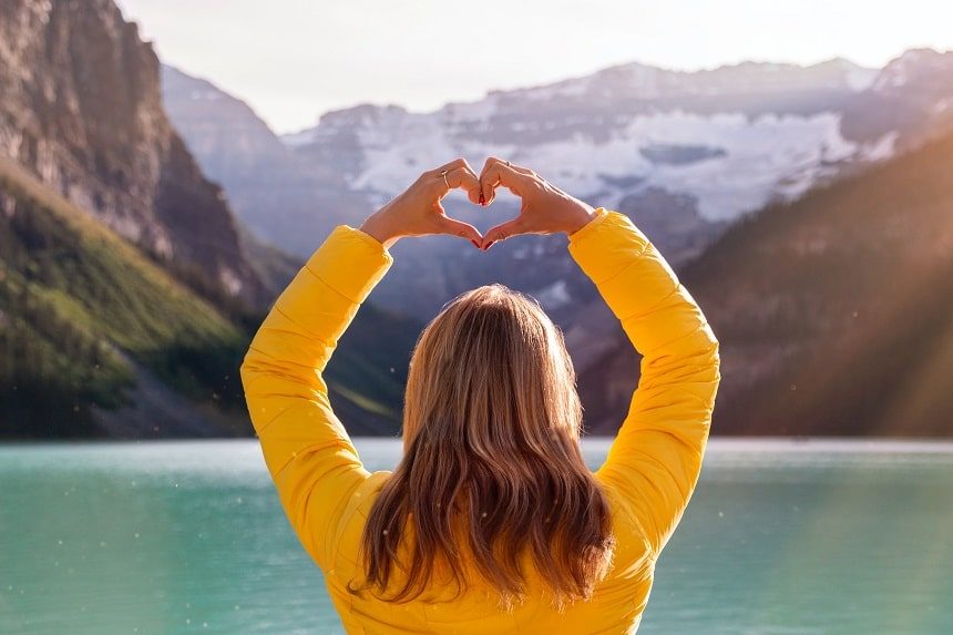 Image, blonde woman in a yellow jacket facing away from the camera and holding her hands in a heart shape above her head